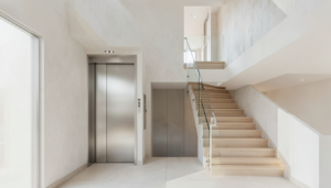 Compact residential elevator entrance beside a light wood staircase in a modern home